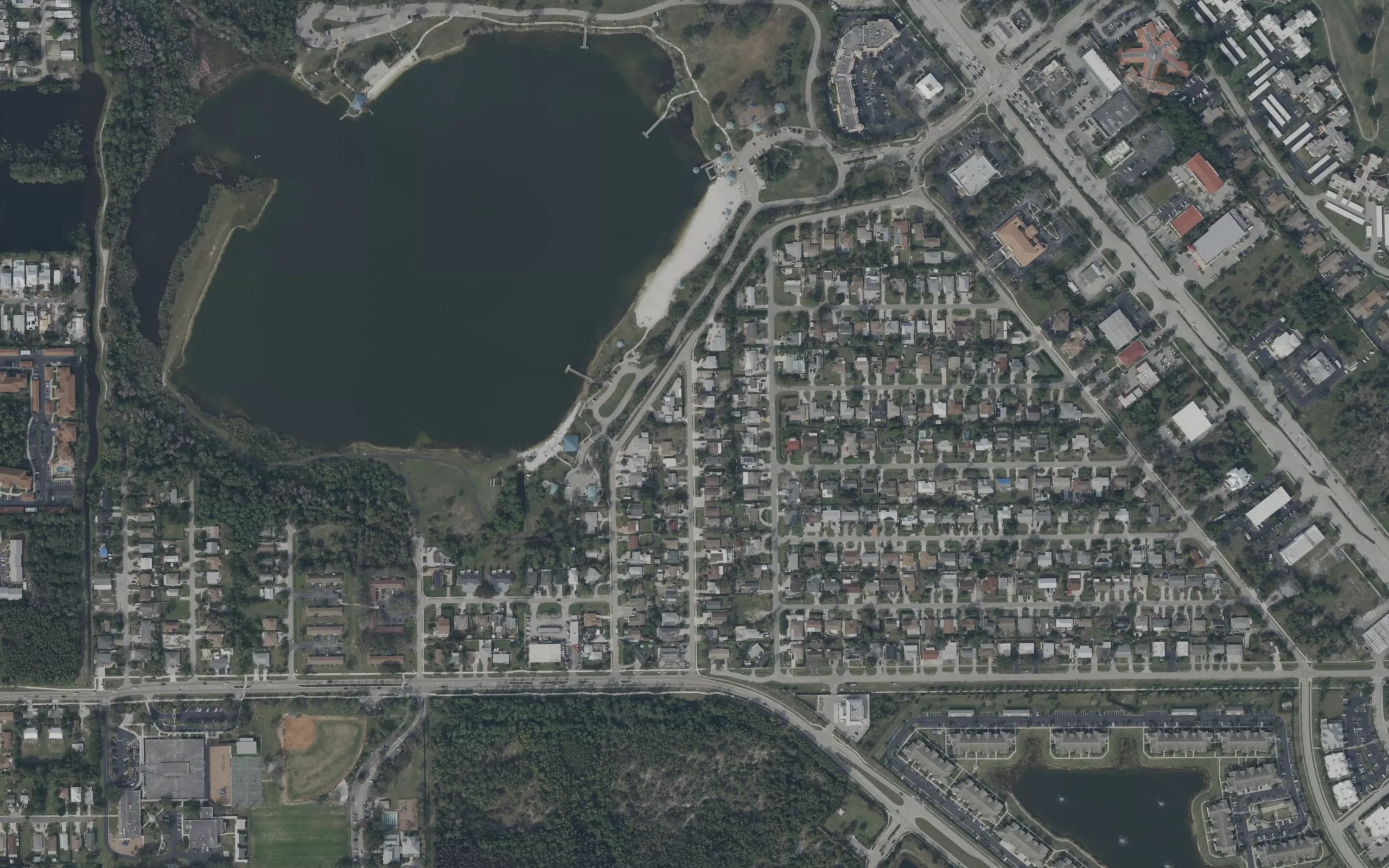 Satellite view of a Florida community: rows of single-family homes on a grid of streets, with a county park and its lake filling one corner of the frame.